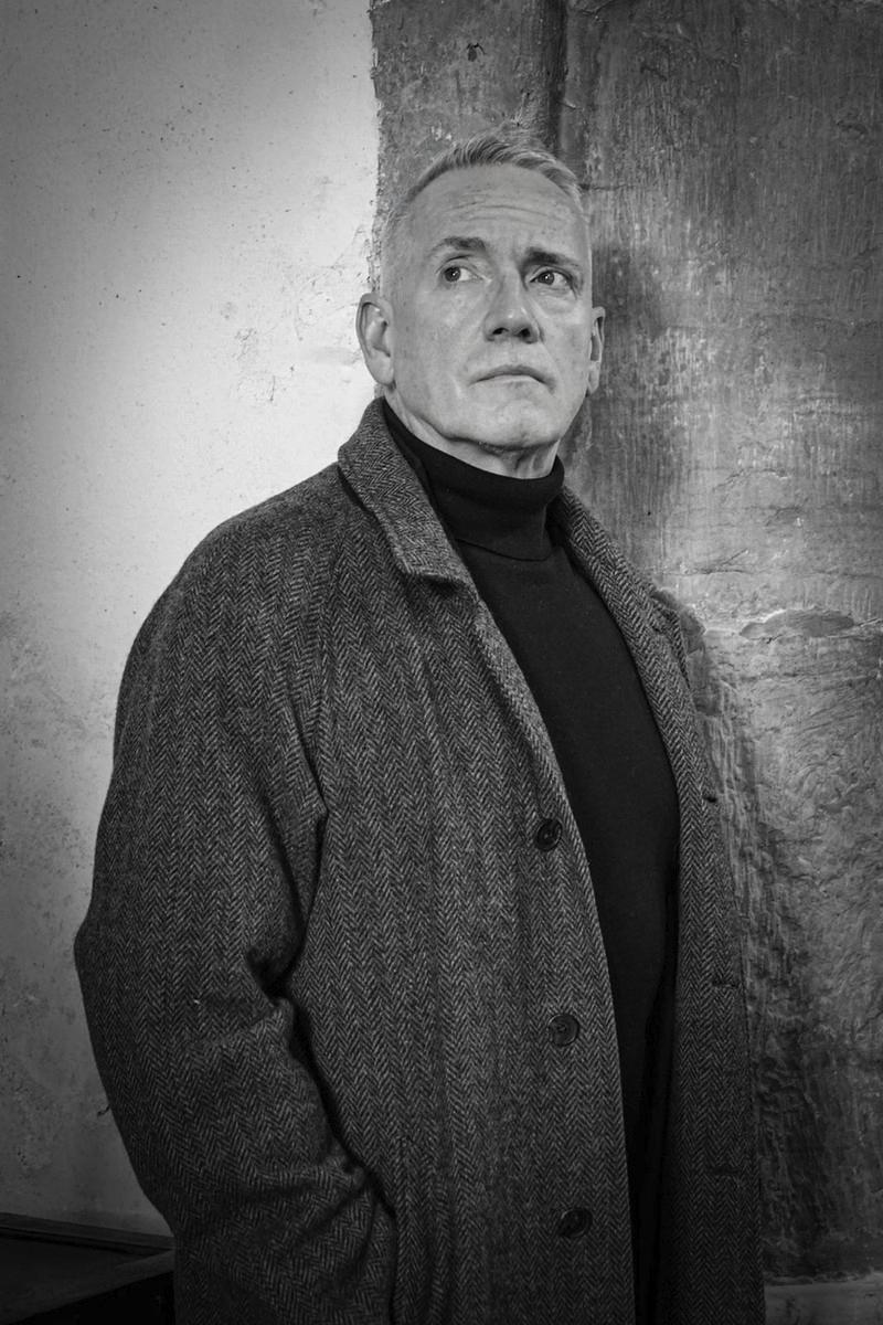 Clifford Beal in black and white, standing beside a stone column